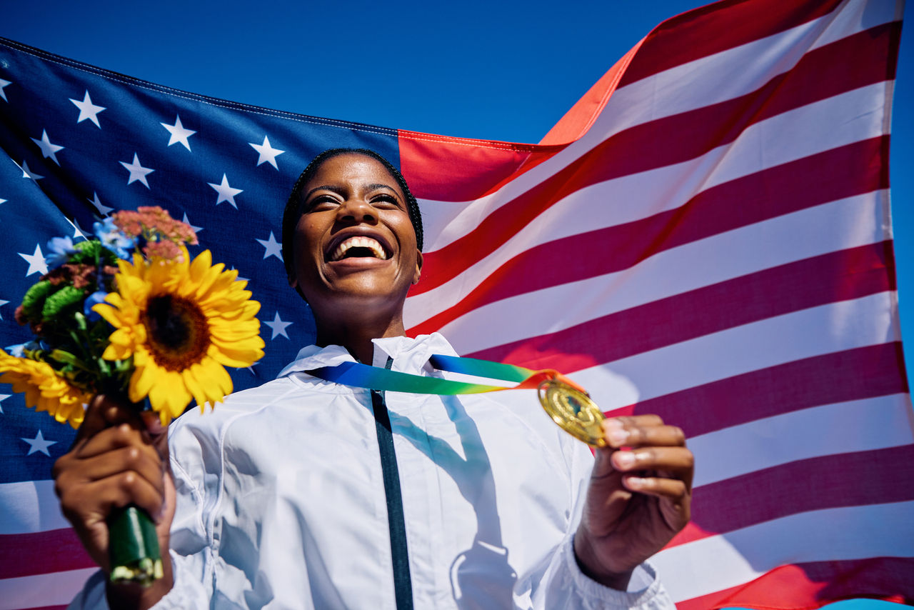 exuberant athlete standing on the podium with an american flag in the background. international sports event concept outdoor portrait.