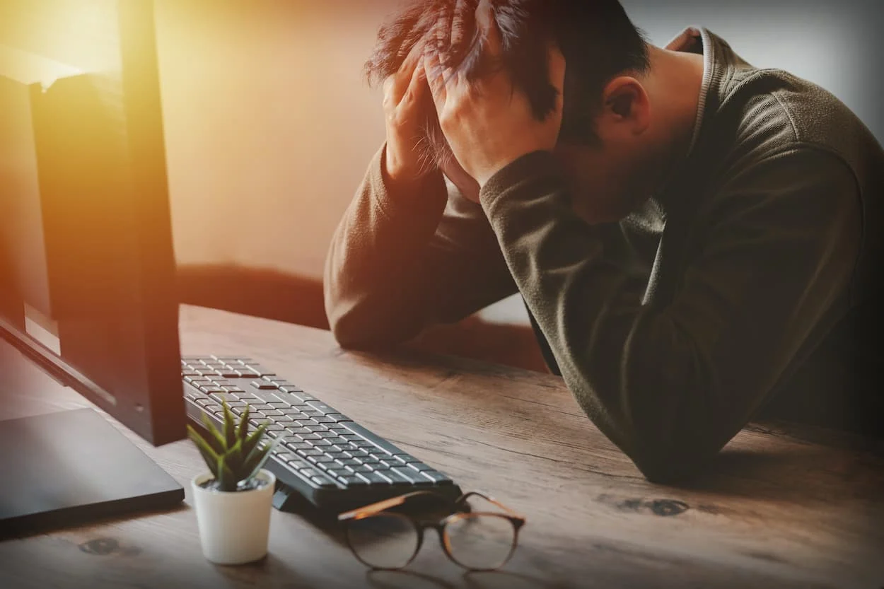 businessman holding his head in front of computer after missing open enrollment (1)