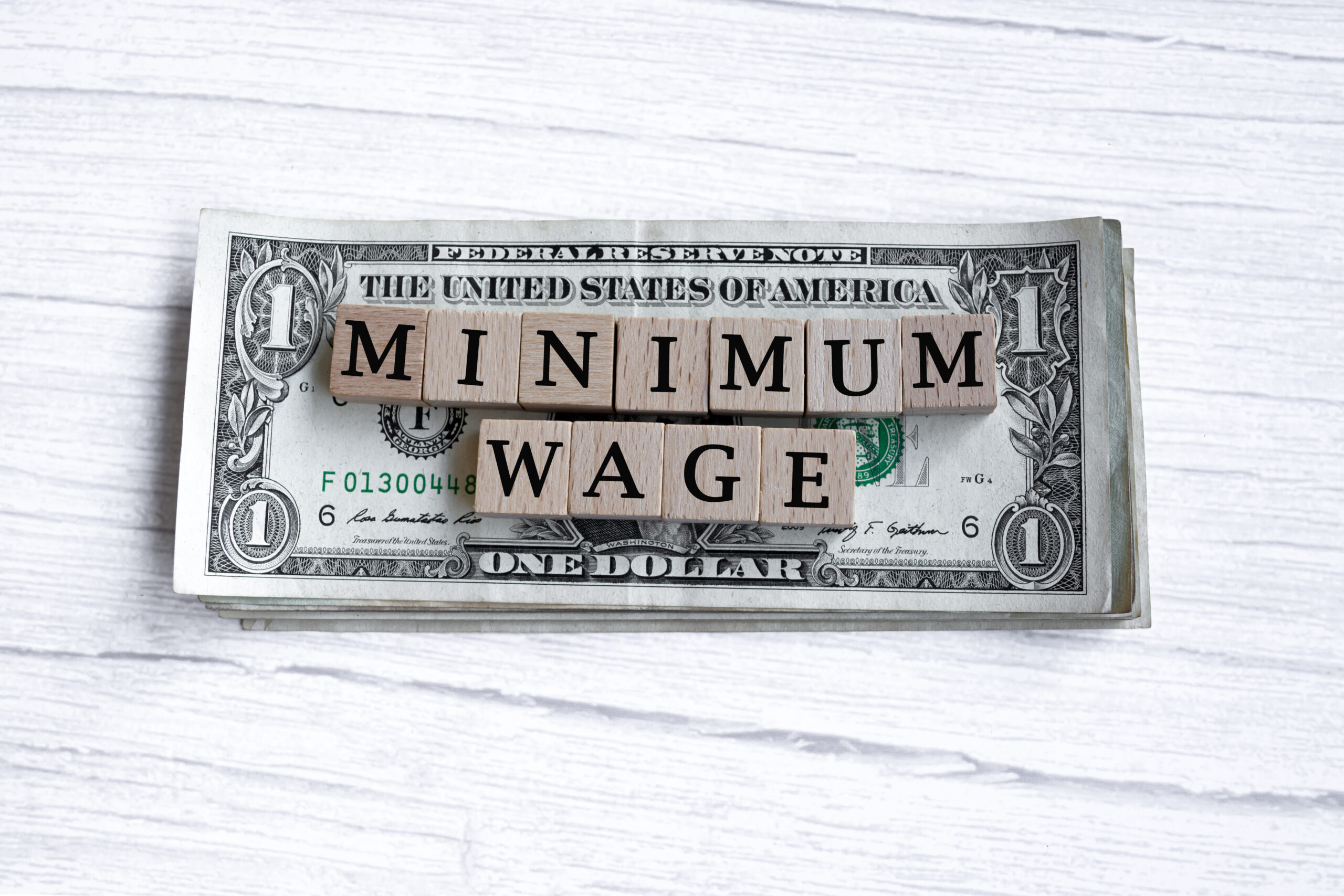 minimum wage word written on wood block with american dollar bills. directly above.